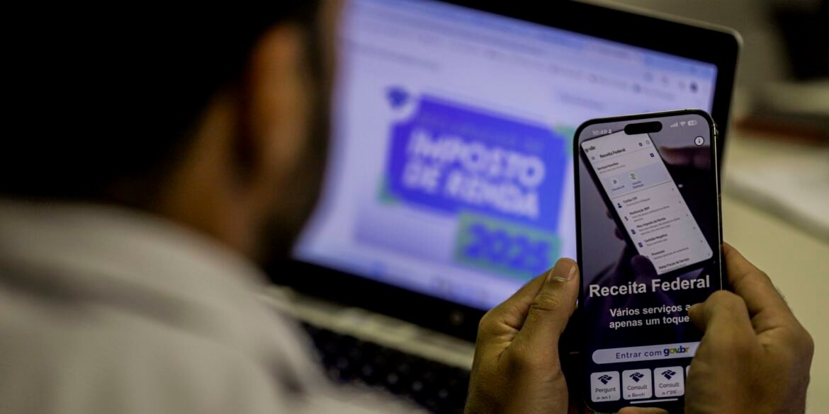 Celular com aplicativo da Receita Federal diante de computador.
