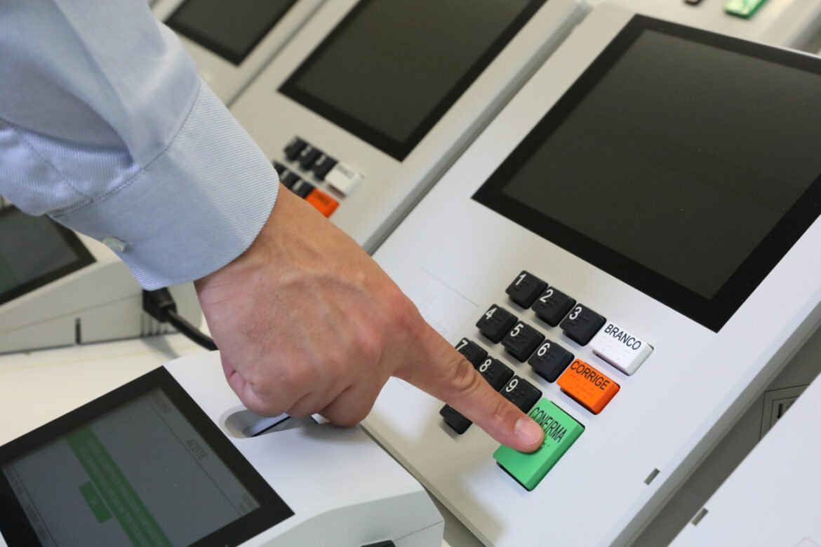 Mão pressiona tecla Confirma de urna eletrônica.
