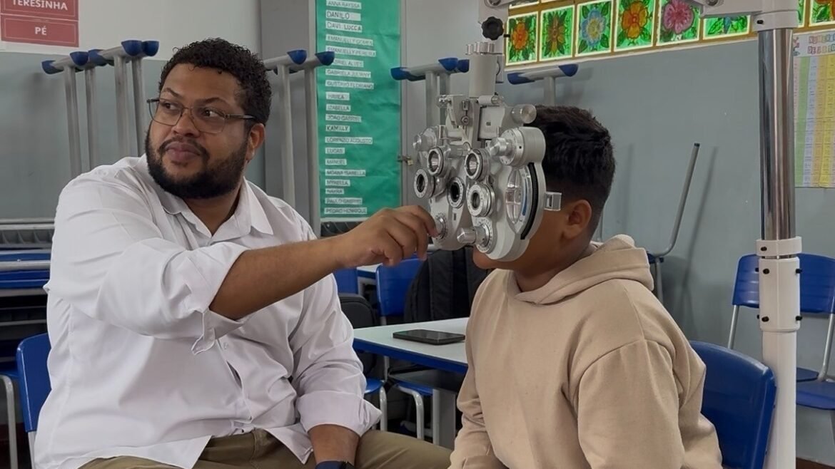 Exames de vista em escola de Goiânia: profissional ajusta equipamento diante de estudante